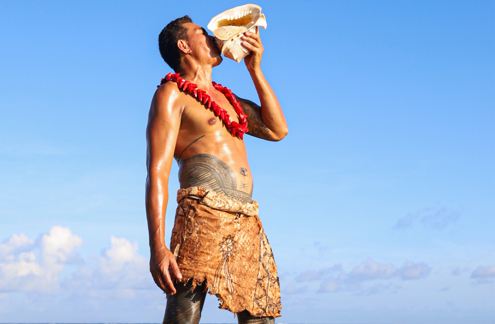 Man in Samoan traditional dress blowing conch shell at CHOGM joint forum opening ceremony